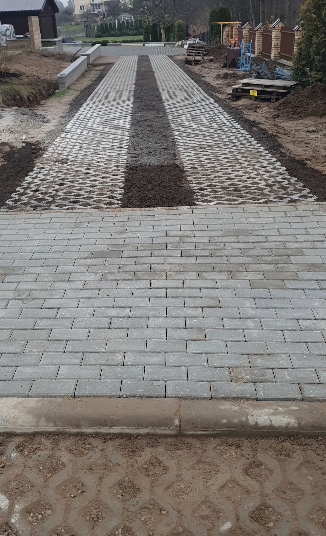 Ścieżka z szarej kostki brukowej w Wasilkowie, z fragmentami ażurowej kostki wypełnionej ziemią. Widok z góry, ukazujący postęp prac.