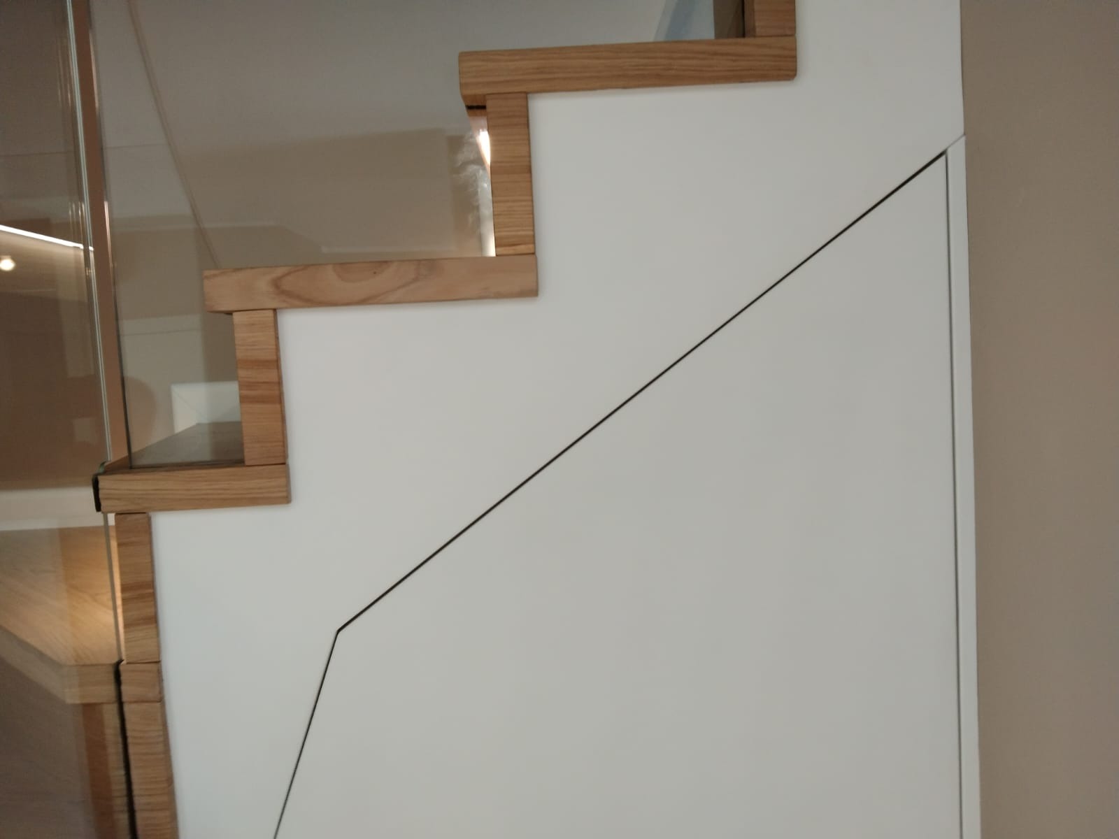 Nowoczesne schody drewniane z białymi panelami i szklaną balustradą, widoczne trzy stopnie z bliska.