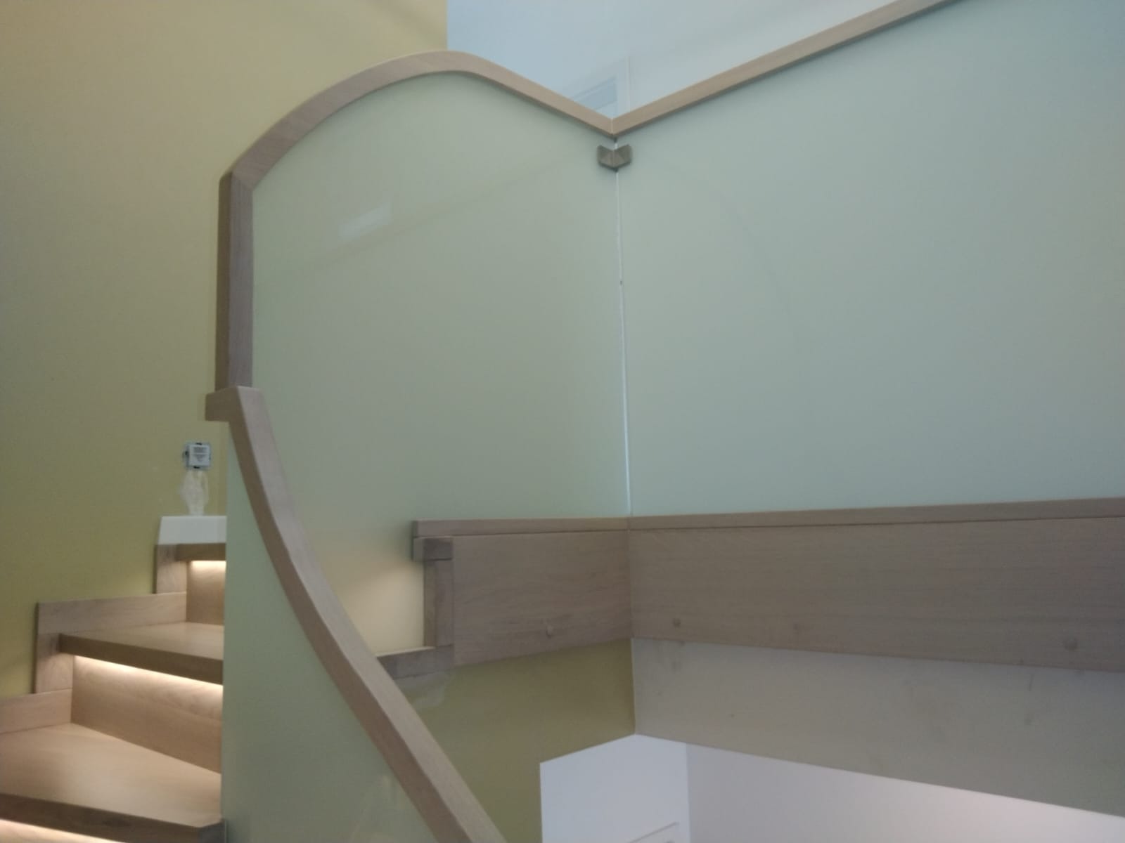 Klatka schodowa z podświetlanymi stopniami, balustradą ze szkła i drewnianymi elementami wykończeniowymi, widoczna z boku.