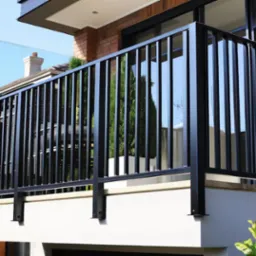 Czarna balustrada z pionowych profili na balkonie nowoczesnego domu z ceglaną elewacją i szklanym panelem bocznym.