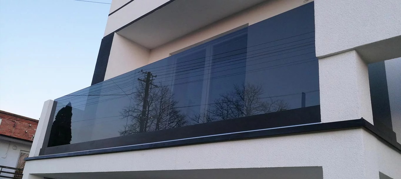 Balkon z nowoczesną szklaną balustradą, widok z dołu, odbicie drzew i słupa energetycznego w szkle.