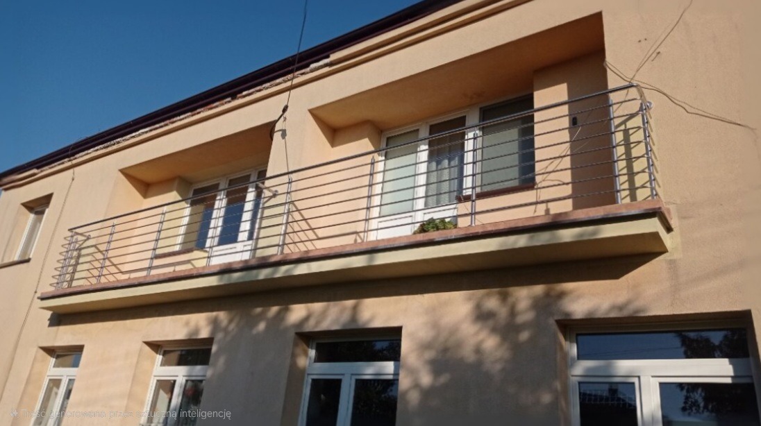 Narożny balkon w budynku mieszkalnym z prostą, poziomą balustradą ze stali nierdzewnej, widok z dołu na tle błękitnego nieba.