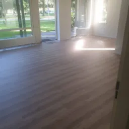 Nowo ułożone panele podłogowe w jasnym pokoju z dużymi oknami wychodzącymi na zieleń na zewnątrz.