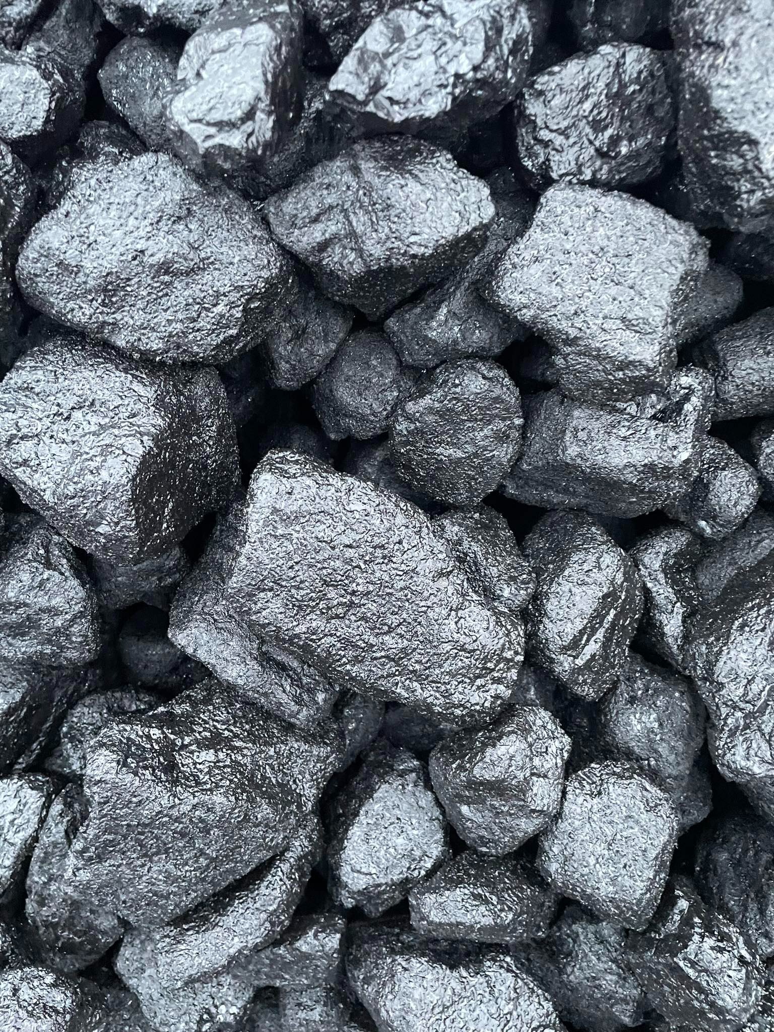 Błyszczące bryły antracytu o nieregularnych kształtach, ułożone blisko siebie, z widoczną fakturą powierzchni i refleksami światła.
