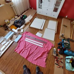 Euroserwis Serhii Zalevskyi - Rozpakowane elementy białej szafy z instrukcją, śrubami i narzędziami na podłodze wyłożonej panelami, przygotowane do montażu.