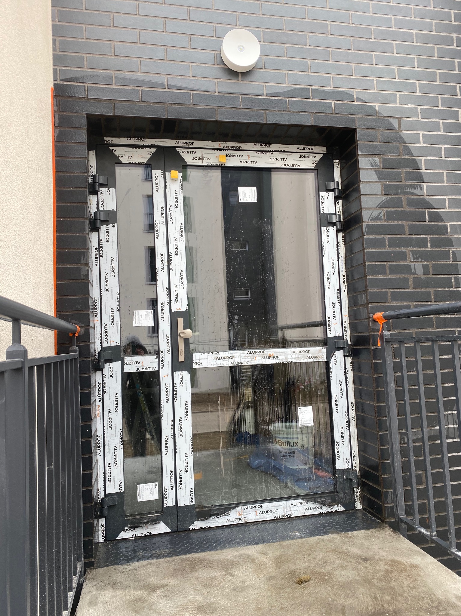 Montaż nowoczesnych, aluminiowych drzwi balkonowych z widocznymi etykietami producenta w Bielsku-Białej, na tle grafitowej ściany z cegły klinkierowej i metalowej balustrady.