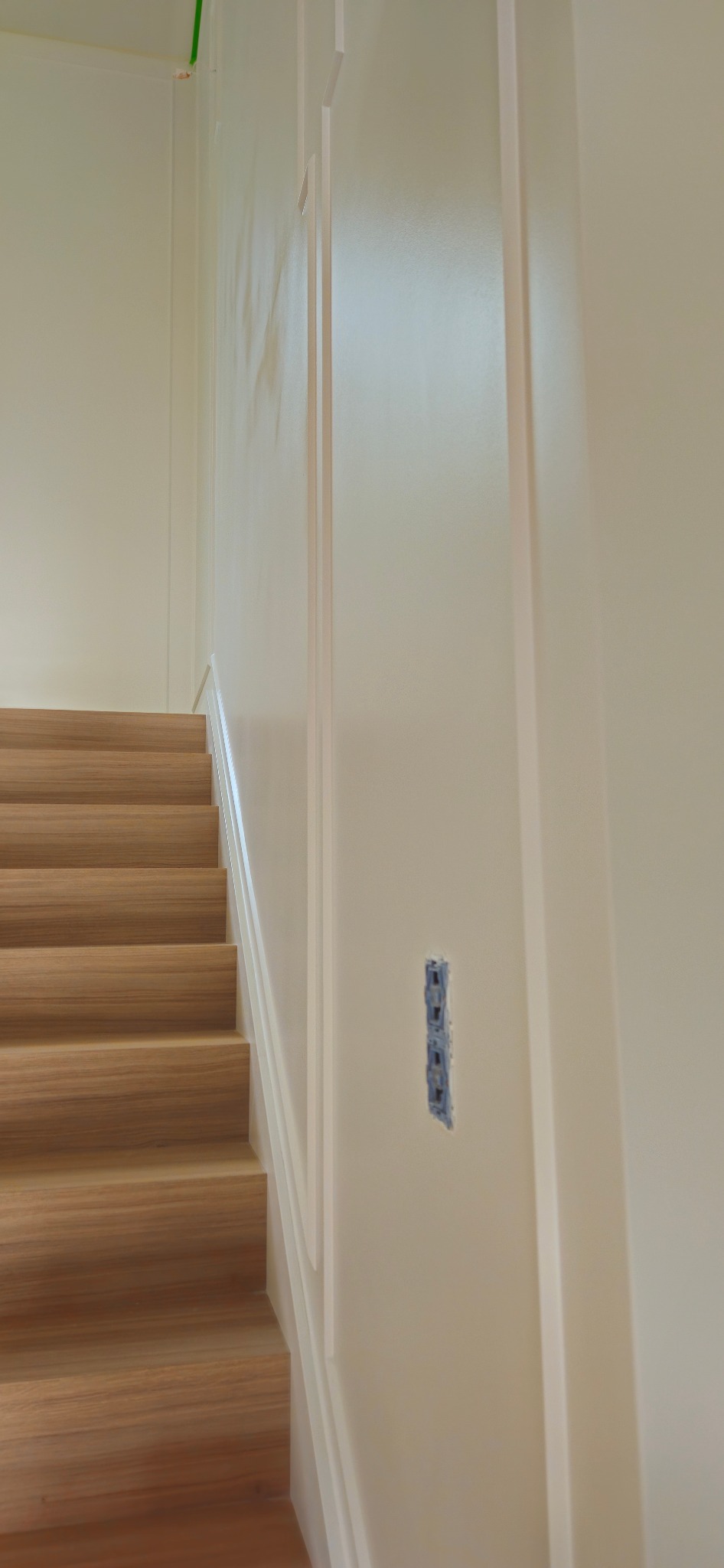 Świeżo pomalowana ściana przy schodach z widocznym miejscem na gniazdko elektryczne przed montażem.