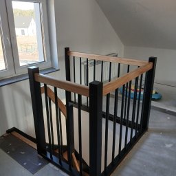 MatWood Usługi Stolarskie - Nowoczesna, czarno-drewniana balustrada schodowa z jasnym drewnem, widok z góry, surowe wykończenie podłogi, duże okno w tle z widokiem na dom.