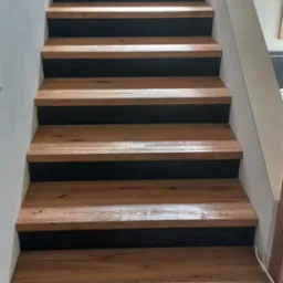 Nowoczesne schody z drewnianymi stopniami i czarnymi podstopnicami, widok z dołu. Naturalne oświetlenie podkreśla teksturę drewna.