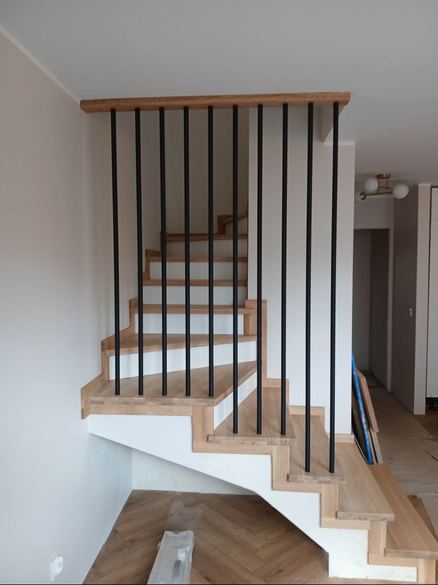 Jasne schody z czarną, minimalistyczną balustradą w nowoczesnym wnętrzu. Widok z dołu, ukazujący detale wykończenia i kontrast kolorystyczny.