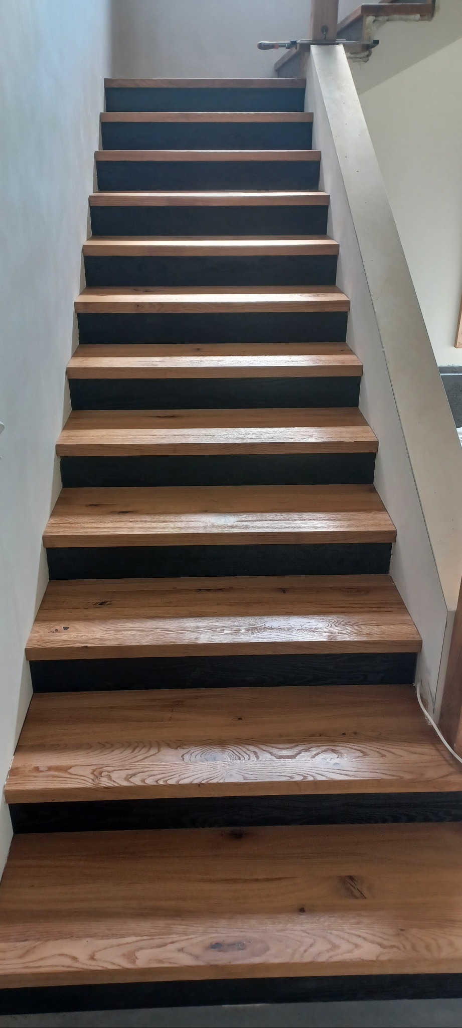 Nowoczesne schody z drewnianymi stopniami i czarnymi podstopnicami, widok z dołu. Naturalne oświetlenie podkreśla teksturę drewna.