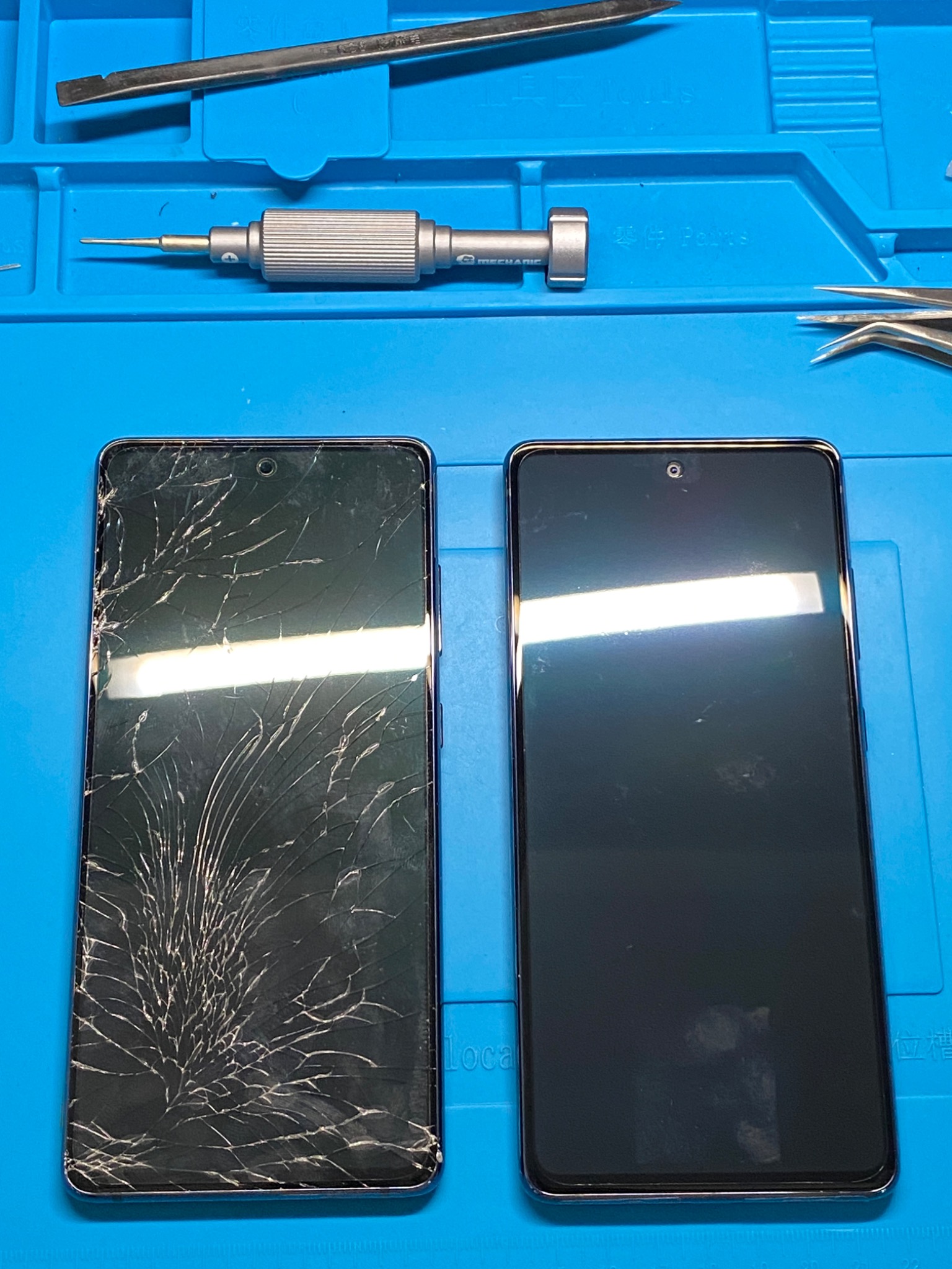 Dwa smartfony leżące obok siebie na niebieskiej macie serwisowej. Jeden ze stłuczoną szybką, drugi z nową, czystą szybką. Nad nimi narzędzia serwisowe: penseta, wkrętak.