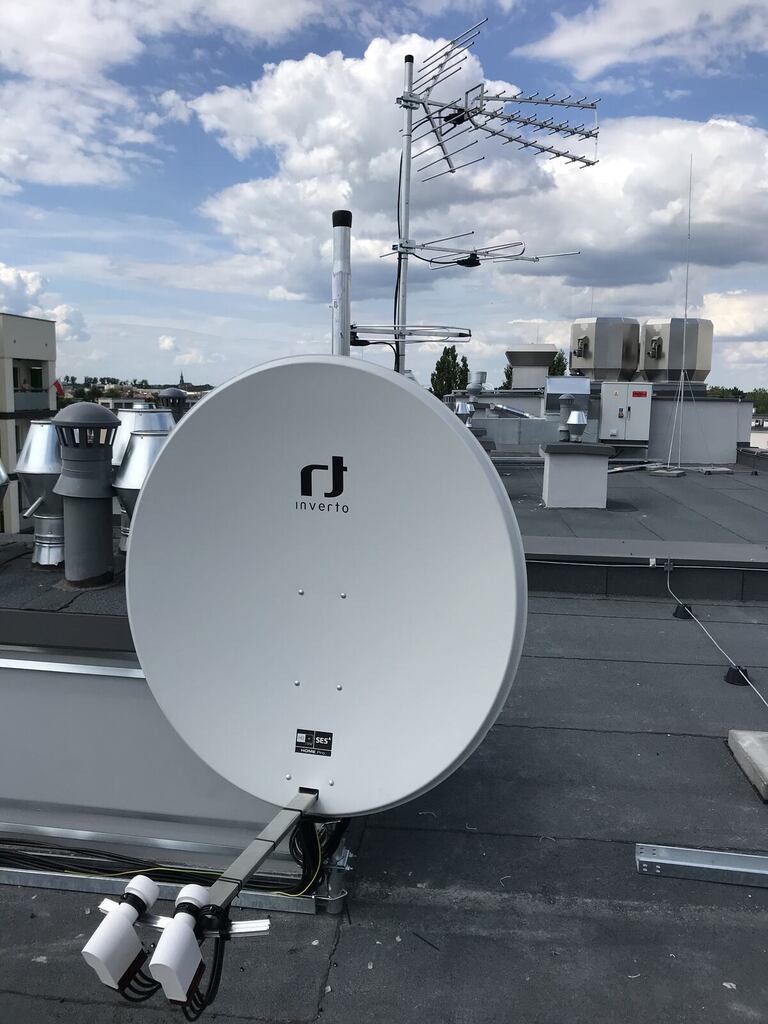Antena satelitarna Invertro i antena naziemna na dachu budynku, widok z dołu, błękitne niebo z chmurami w tle.