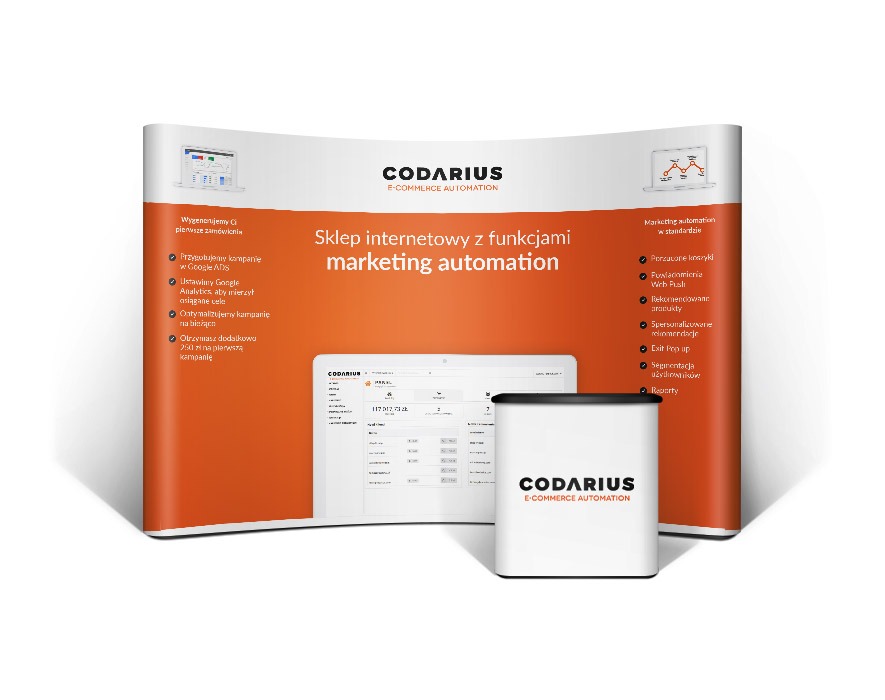 Stoisko reklamowe z panelem prezentującym funkcje sklepu internetowego z automatyzacją marketingu, widoczny tablet z interfejsem sklepu, całość w kolorystyce pomarańczowo-białej z logo firmy.