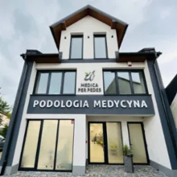 Elewacja budynku z napisem 'PODOLOGIA MEDYCYNA' oraz logo 'MEDICA PER PEDES' przedstawiającym stopy z liściem, widoczne wejście do kliniki z osobą w środku.