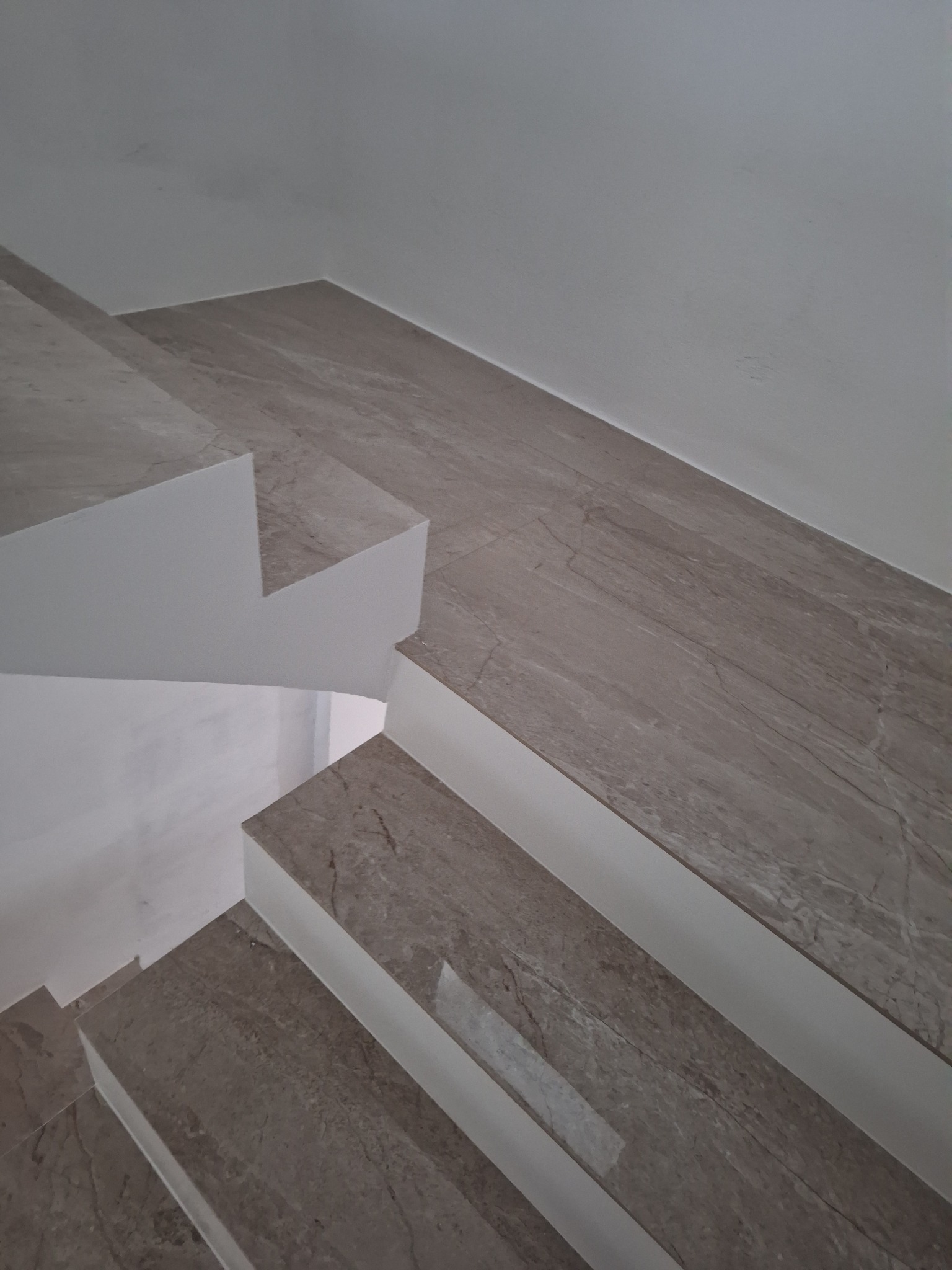 Schody wykończone płytkami imitującymi marmur, widok z góry, jasne ściany.