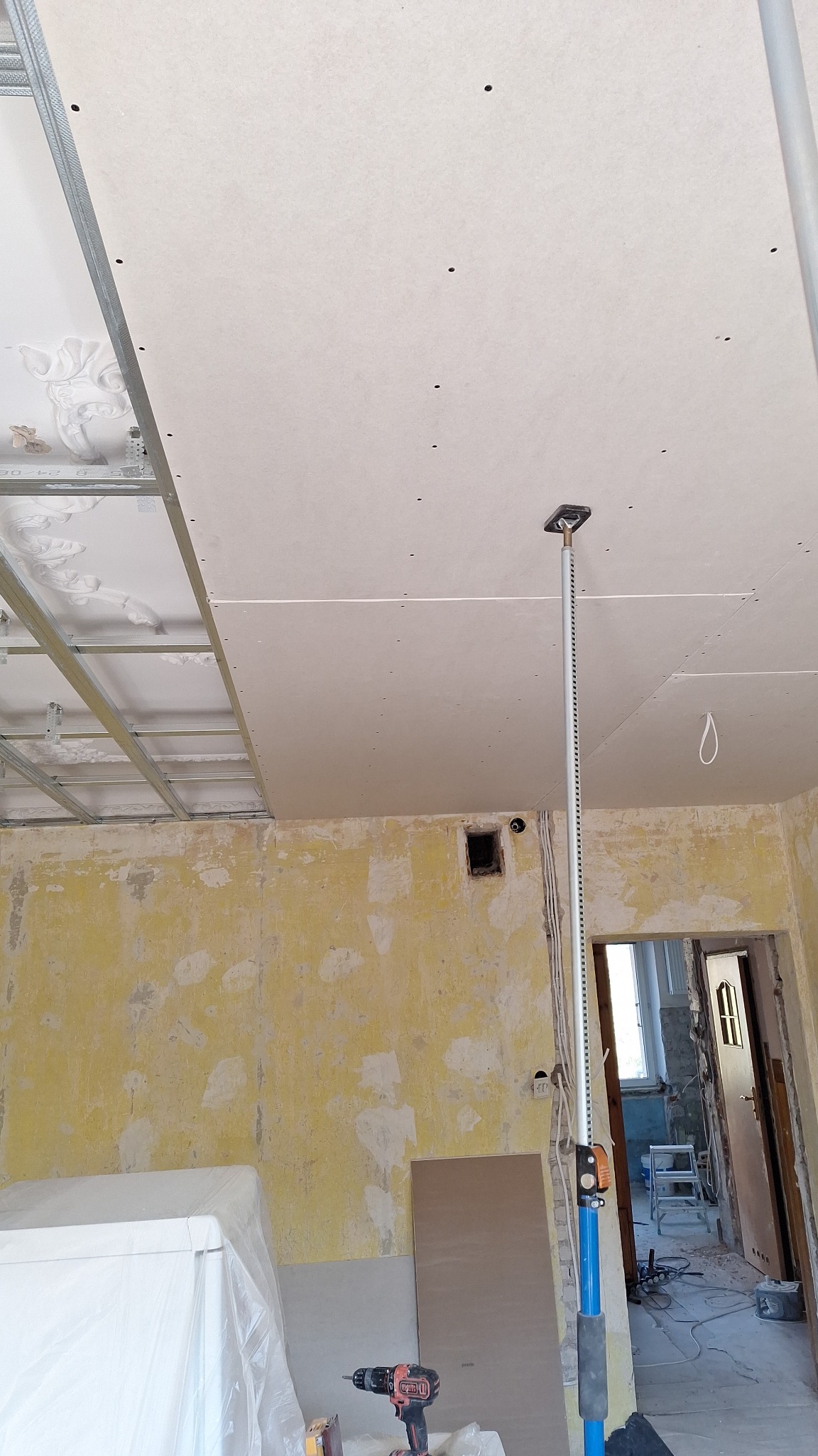 Montaż sufitu podwieszanego z płyt karton gips w trakcie remontu mieszkania w Białymstoku, widoczny stelaż, płyty z otworami oraz podpórka teleskopowa.