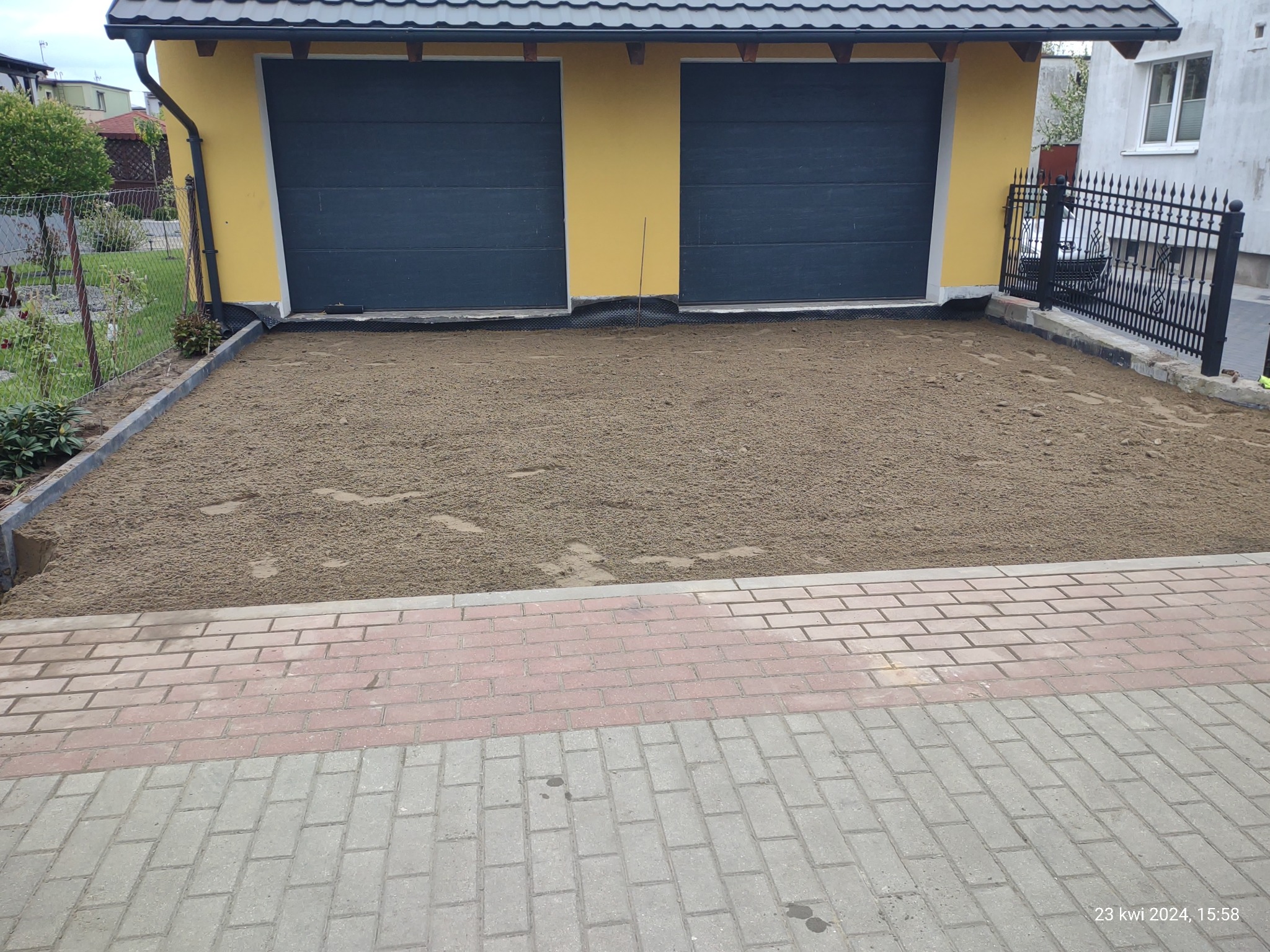 Przygotowany teren pod kostkę brukową z widocznymi obrzeżami i podsypką, garaż w tle.