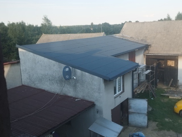 Widok z góry na budynek z nowym, ciemnoszarym dachem w Bytomiu, z widoczną anteną satelitarną na ścianie i budynkami gospodarczymi w tle. Dach o płaskiej powierzchni.