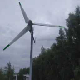 Mała turbina wiatrowa z trzema białymi łopatami z zielonymi końcówkami, zamontowana na szarym maszcie, na tle pochmurnego nieba i drzew.