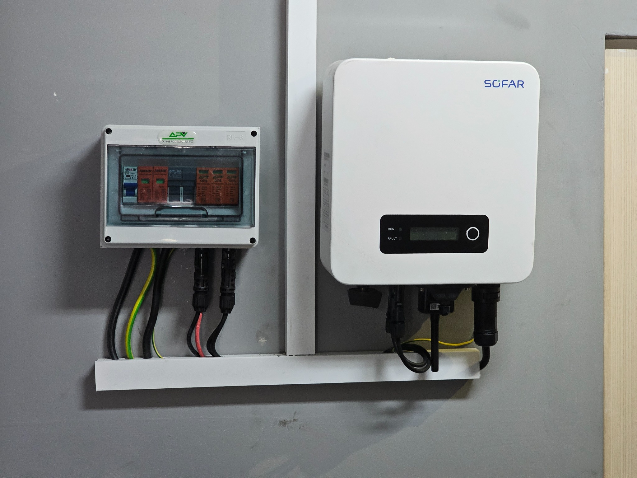 Biała skrzynka z bezpiecznikami i falownik Sofar zamontowane na szarej ścianie, kable w listwie przypodłogowej.