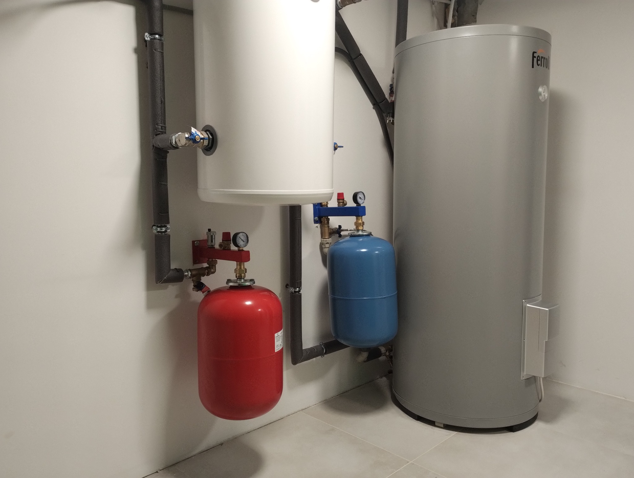 Instalacja dwóch zbiorników buforowych: białego i szarego, z podłączonymi naczyniami przeponowymi w kolorach czerwonym i niebieskim, oraz rurami w izolacji.