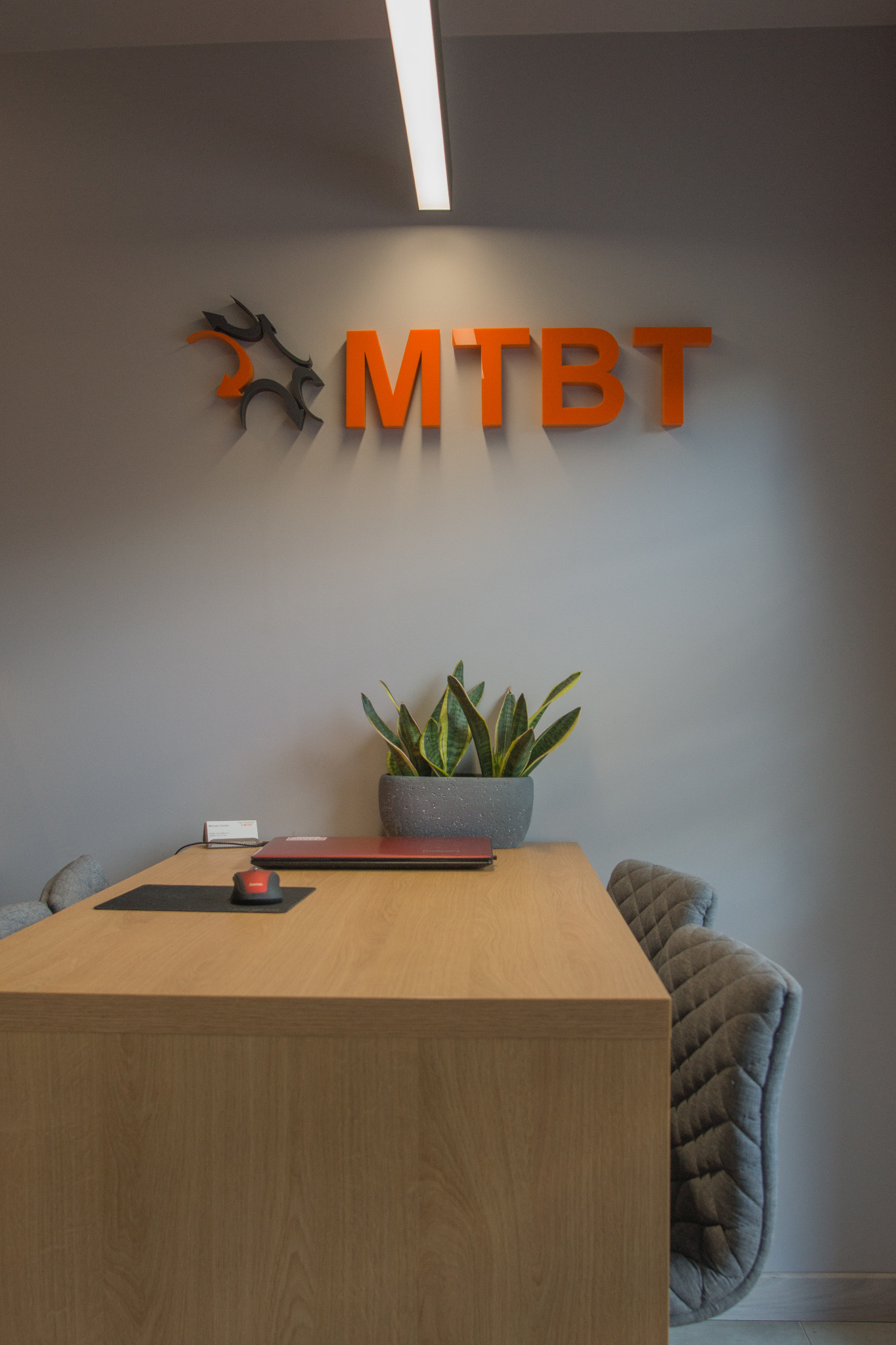Recepcja biura z logo MTB na ścianie, biurkiem z laptopem i myszką oraz rośliną doniczkową.