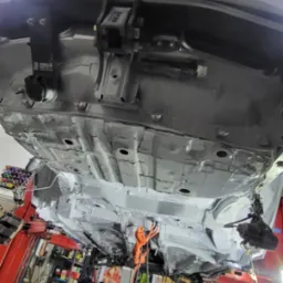 Widok od dołu na podwozie samochodu Toyota, po zabezpieczeniu antykorozyjnym, na podnośniku w warsztacie, z widocznymi elementami zawieszenia i narzędziami w tle.