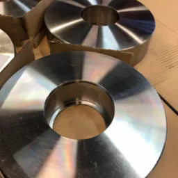 Metalowe pierścienie z otworem w środku, ułożone na kartonowym podłożu, widoczne ślady obróbki i refleksy świetlne na powierzchni.