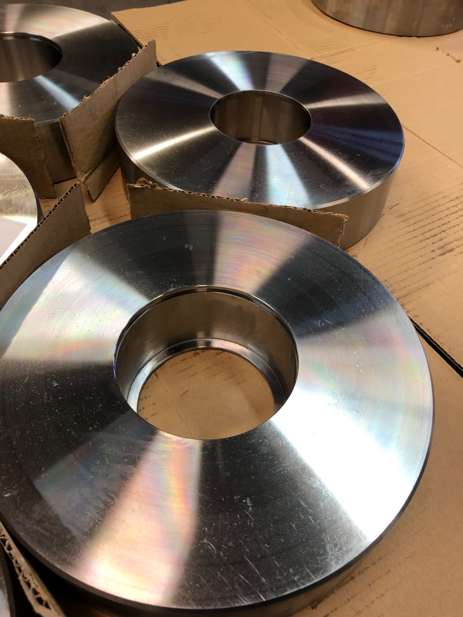 Metalowe pierścienie z otworem w środku, ułożone na kartonowym podłożu, widoczne ślady obróbki i refleksy świetlne na powierzchni.