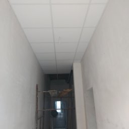 Valeria BUD Vasyl Trachuk - Korytarz w trakcie wykańczania, widoczny rusztowanie, sufit kasetonowy w trakcie montażu, ściany częściowo otynkowane.