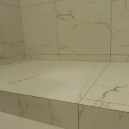 Wykończona powierzchnia brodzika z białych płytek imitujących marmur, z widocznym fragmentem węża odkurzacza na pierwszym planie.