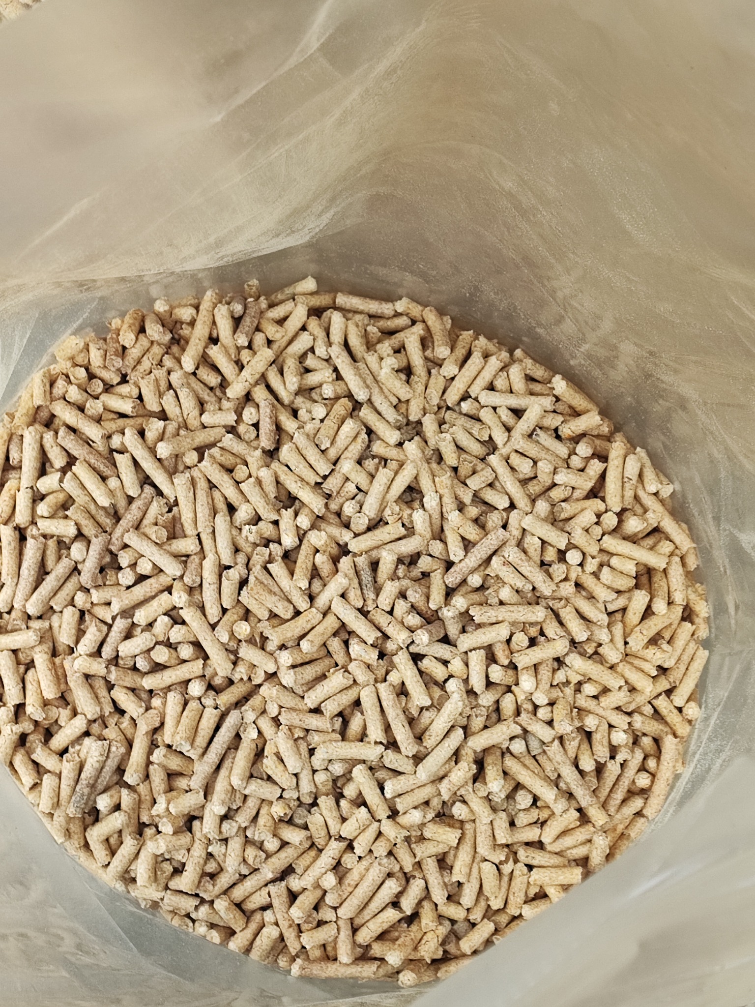 Jasne pellety drzewne w przezroczystym worku, widoczne z góry, z lekkim efektem rozmycia