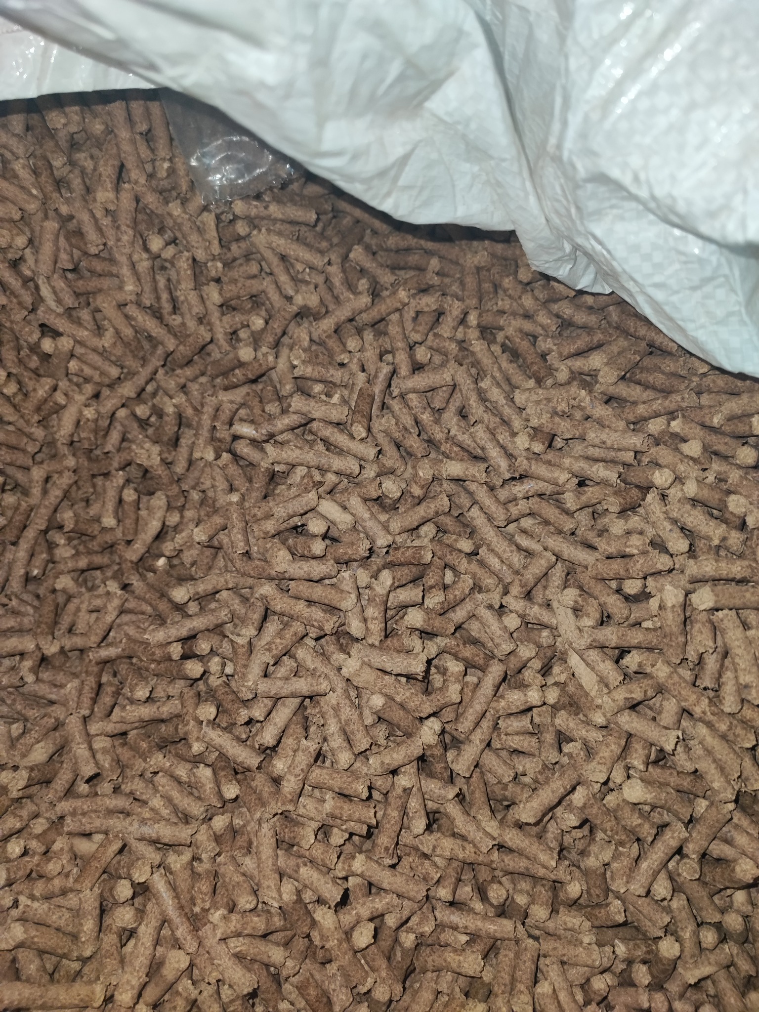 Wypełniony worek z jasnego tworzywa brązowymi peletami drzewnymi, widoczne nieregularne ułożenie i drobne nierówności w strukturze peletu.
