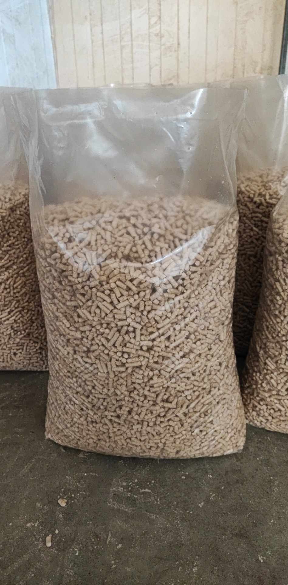 Wypełniony pelletem przezroczysty worek foliowy, widoczne inne podobne worki w tle, na szarym podłożu.