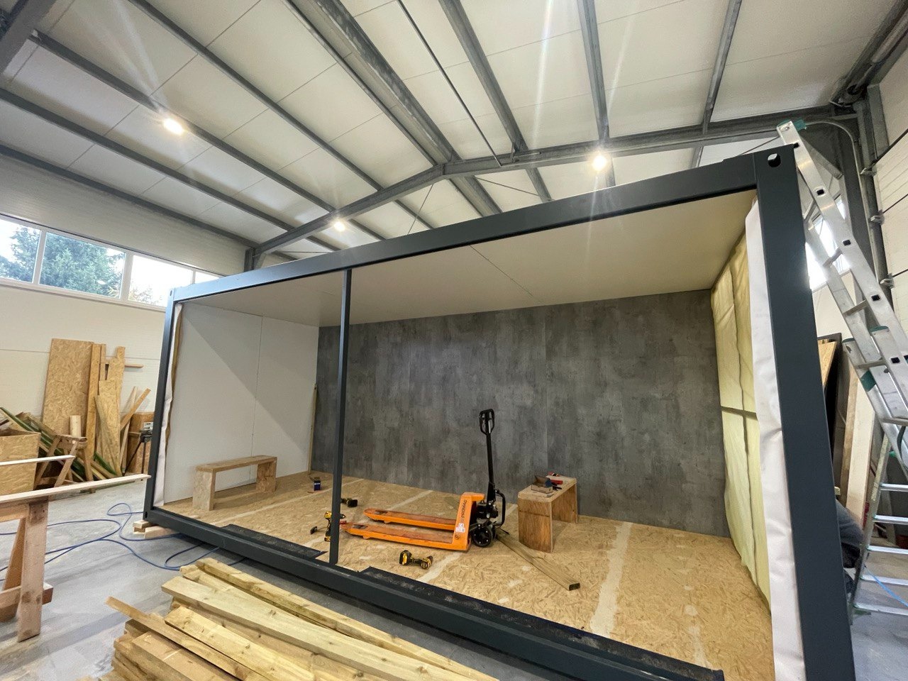 Wnętrze powstającego domu w Bolesławcu, widoczny szkielet konstrukcji, podłoga z płyt OSB, częściowo ocieplone ściany, paleciak i narzędzia budowlane.