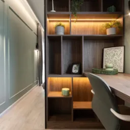 Biurko z wbudowanym regałem oświetlonym od wewnątrz, zielona ściana z dekoracyjnymi listwami, drewniana podłoga, nowoczesny styl.