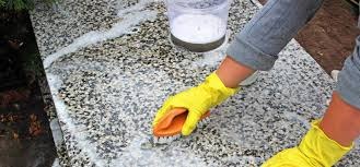 Czyszczenie powierzchni z drobnego kamienia szczotką i detergentem, widoczne żółte rękawice ochronne i wiadro z roztworem czyszczącym.