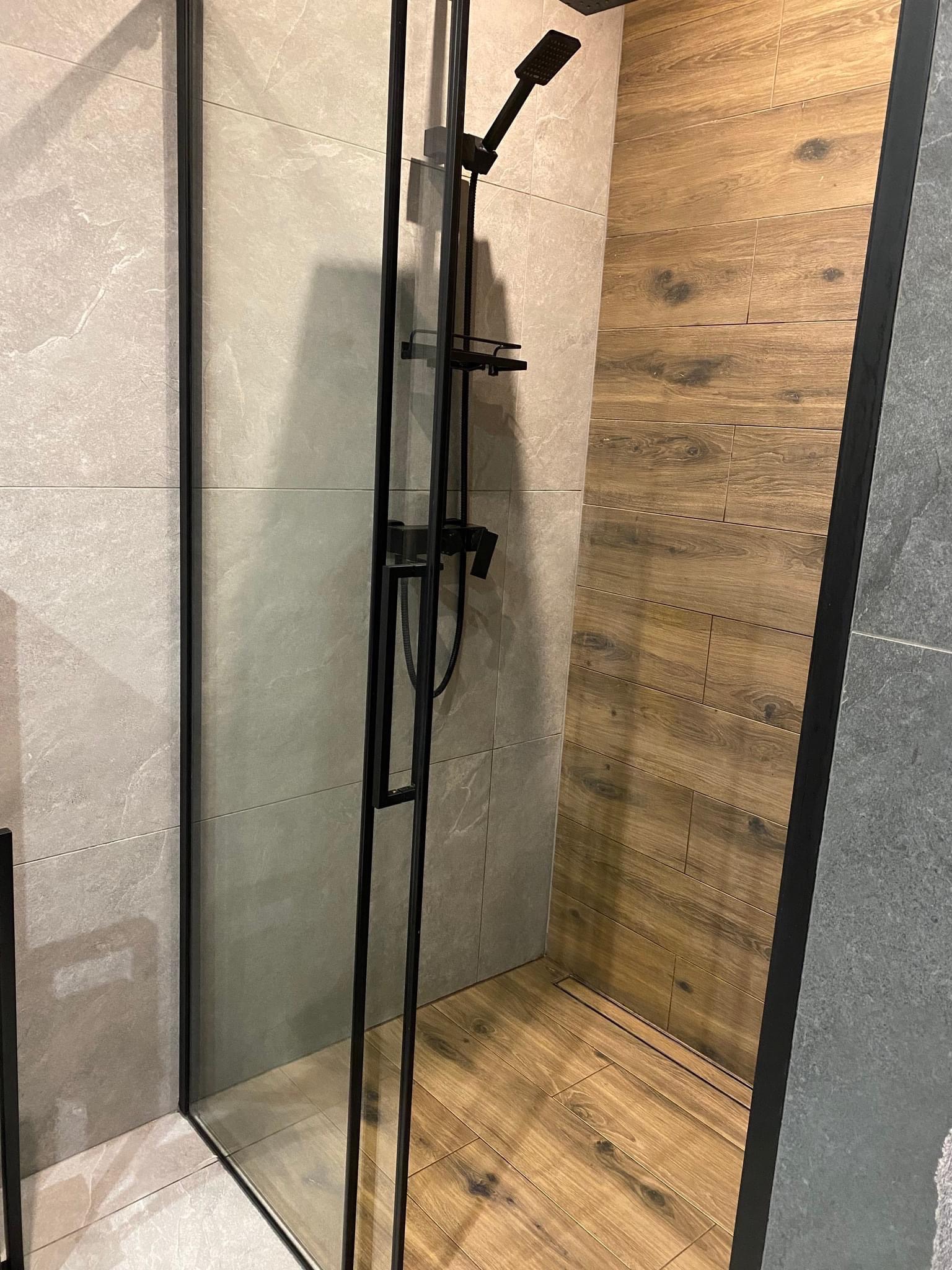 Nowoczesna kabina prysznicowa z czarnymi profilami, wyłożona płytkami imitującymi drewno i szarym kamieniem.