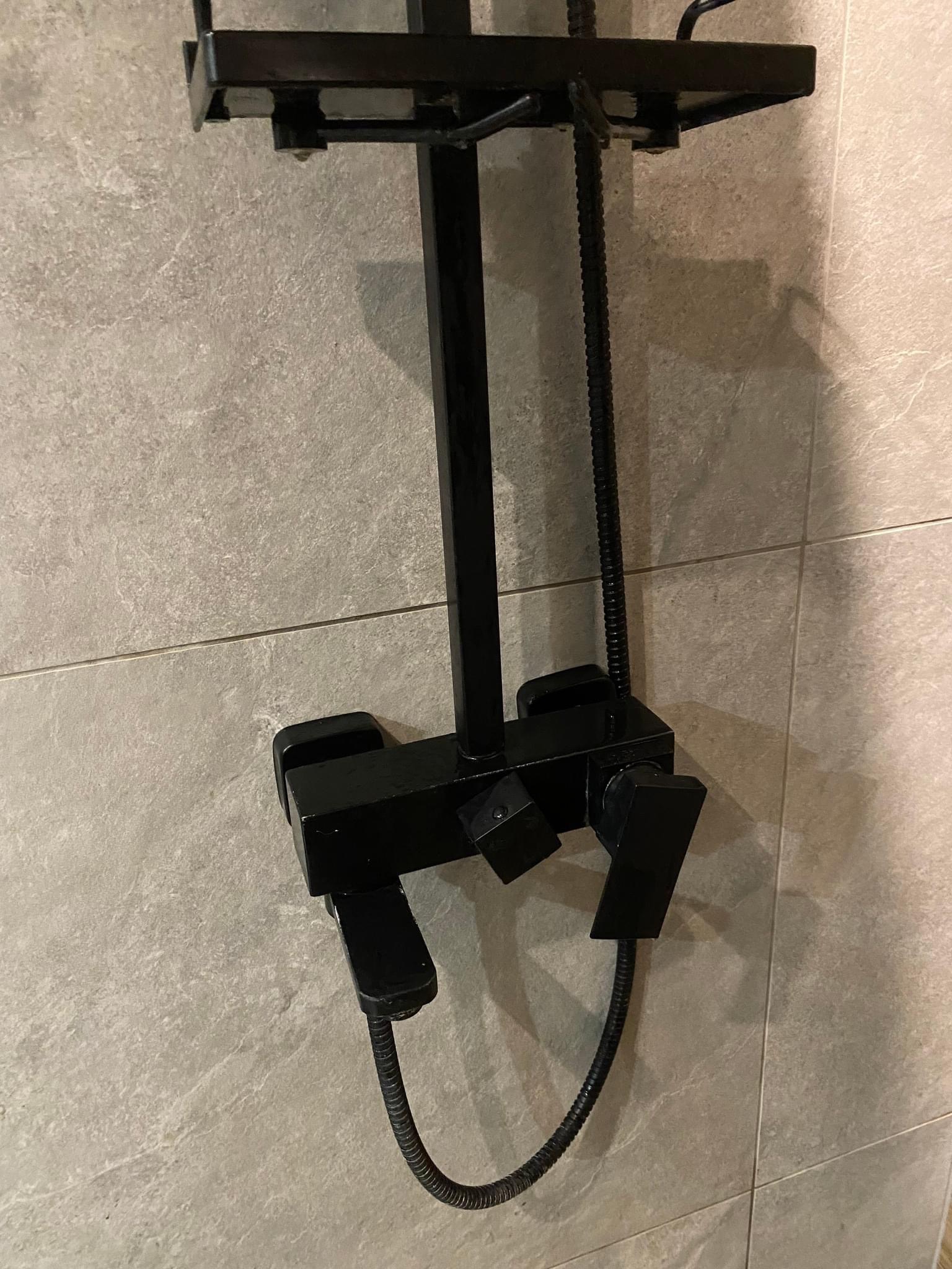 Czarny, nowoczesny zestaw prysznicowy z deszczownicą zamontowany na szarej, kafelkowanej ścianie w łazience w Bytomiu, widok z bliska.