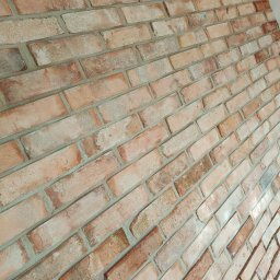 Wykończenie wnętrz i elewacje Machowski Paweł - Dekoracyjna ściana z cegły klinkierowej w odcieniach czerwieni i beżu, z widoczną strukturą i fugami, ułożona pod kątem.