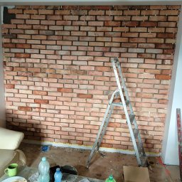 Wykończenie wnętrz i elewacje Machowski Paweł - Ściana z cegieł klinkierowych w trakcie montażu, widoczne krzyżyki dystansowe, drabina aluminiowa i bałagan na podłodze.