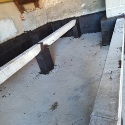 Wykończenie wnętrz i elewacje Machowski Paweł - Hydroizolacja fundamentów w piwnicy, z widocznymi betonowymi belkami i fragmentami muru z cegieł i pustaków.