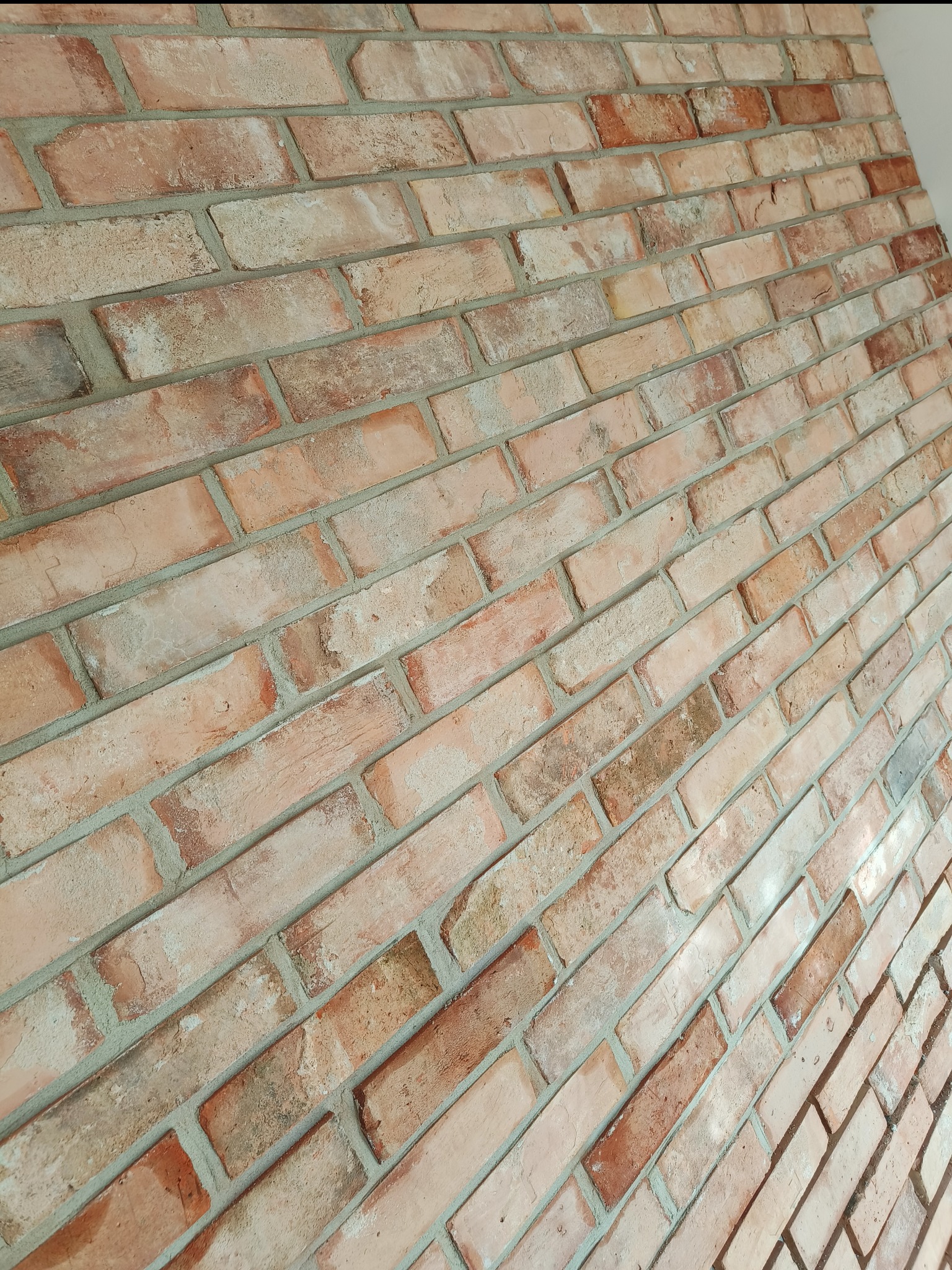 Dekoracyjna ściana z cegły klinkierowej w odcieniach czerwieni i beżu, z widoczną strukturą i fugami, ułożona pod kątem.