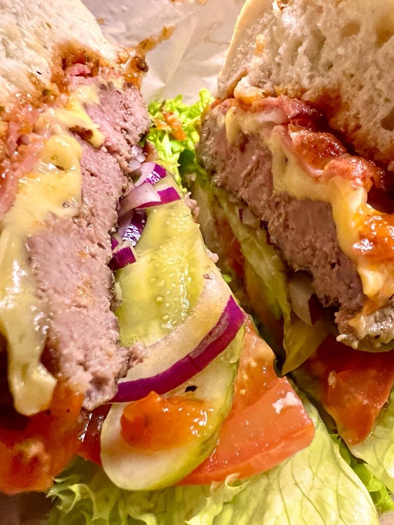 Przekrój burgera z wołowiną, serem, pomidorem, ogórkiem kiszonym, czerwoną cebulą i sałatą, widziany z bliska, z nierównomiernie rozprowadzonym sosem.