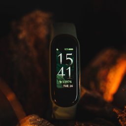 Jan Janota - Smartband z wyświetlaczem pokazującym godzinę 15:41, datę i poziom naładowania baterii, umieszczony na tle kamieni i mchu w ciepłym oświetleniu.