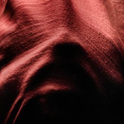 Jan Janota - Abstrakcyjne ujęcie pofałdowanej, czerwono-brązowej tkaniny z głębokimi cieniami, tworzące wrażenie trójwymiarowości i tajemniczości.