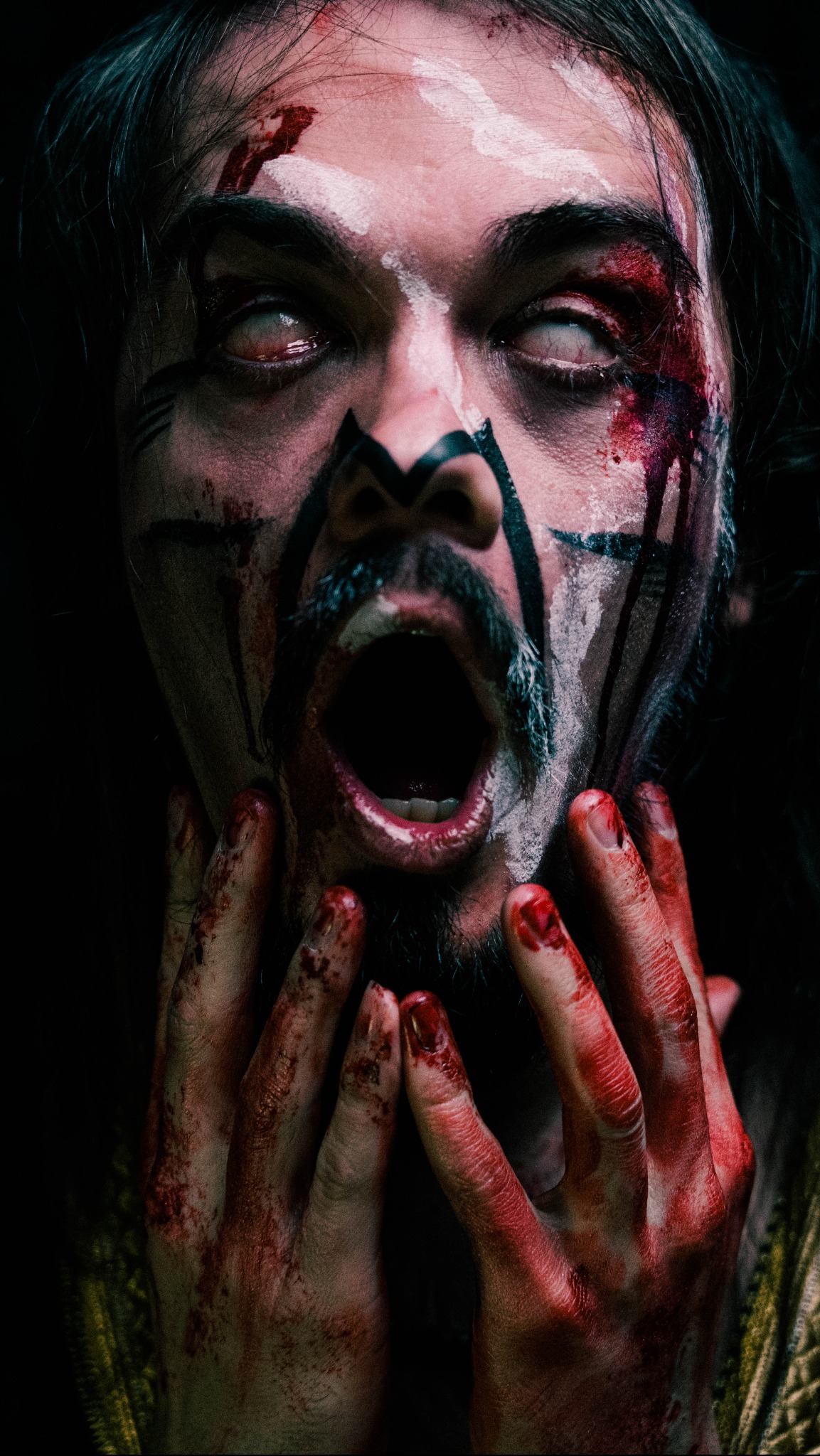 Przerażający portret mężczyzny z białymi soczewkami kontaktowymi, krwią i białymi oraz czarnymi malunkami na twarzy, krzyczącego z rękami splamionymi krwią.