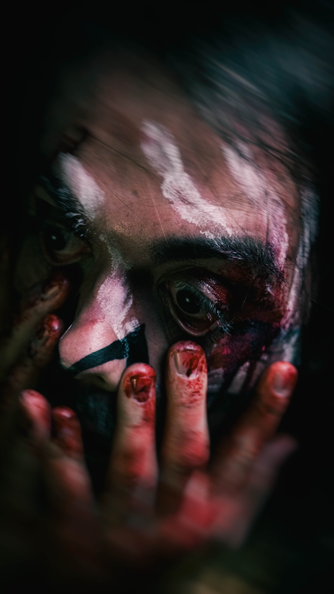 Mężczyzna z krwawym makijażem i pomalowanymi palcami, zbliżenie na twarz i dłonie.