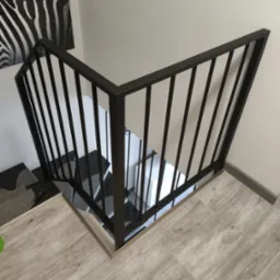 Nowoczesna, czarna balustrada schodowa z pionowych prętów, widoczna z góry, z drewnianymi panelami podłogowymi i dekoracją zebrą na ścianie.